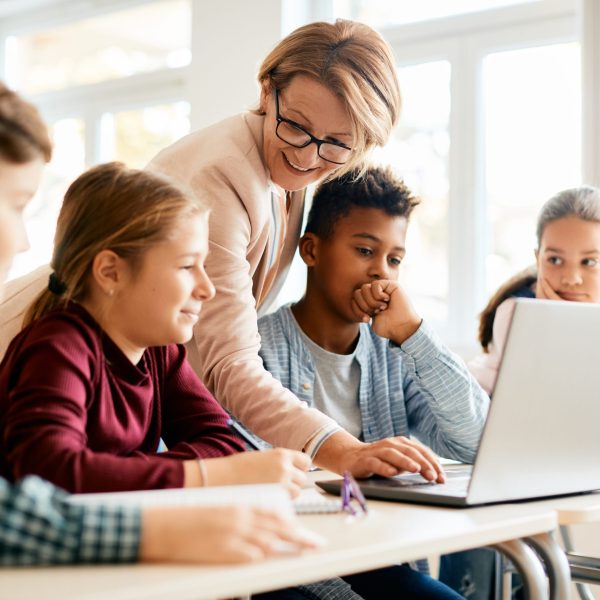 Happy teacher and her students use laptop during computer class at elementary school.